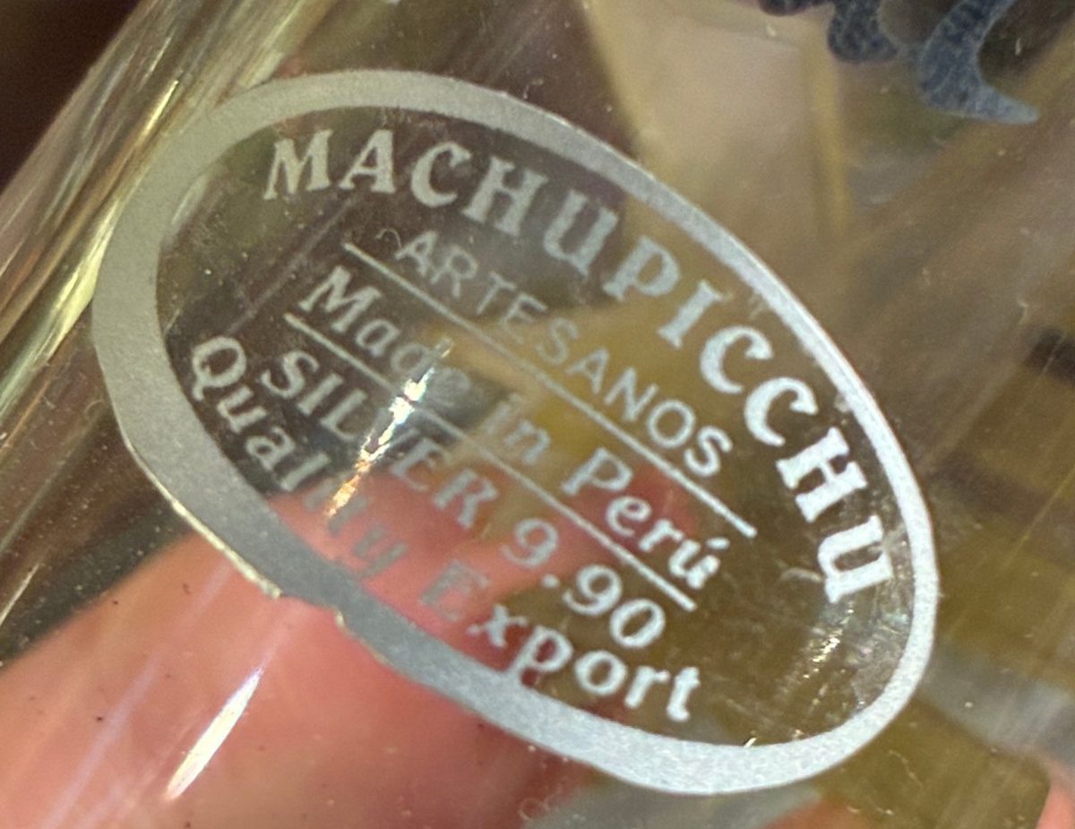 A shop sticker on a glass with silver decoration, reading Machupicchu Artesanos, Made in Perú, Silver 9.90, Quality Export.